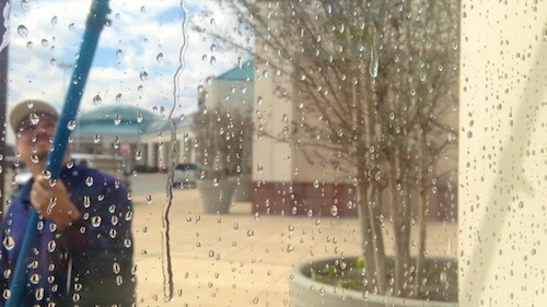 Water droplets on glass as worker cleans window with blue pole